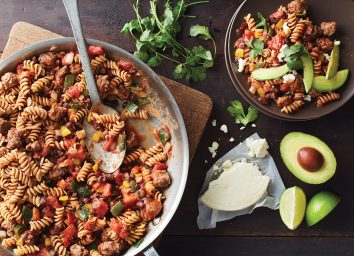 one skillet taco pasta with spoon, cotija cheese, and sliced avocado
